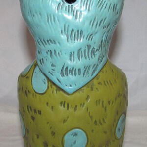 Pu&ograve; includere: Un mug tiki in ceramica con una testa blu e un corpo verde. Il corpo &egrave; decorato con fiori blu.