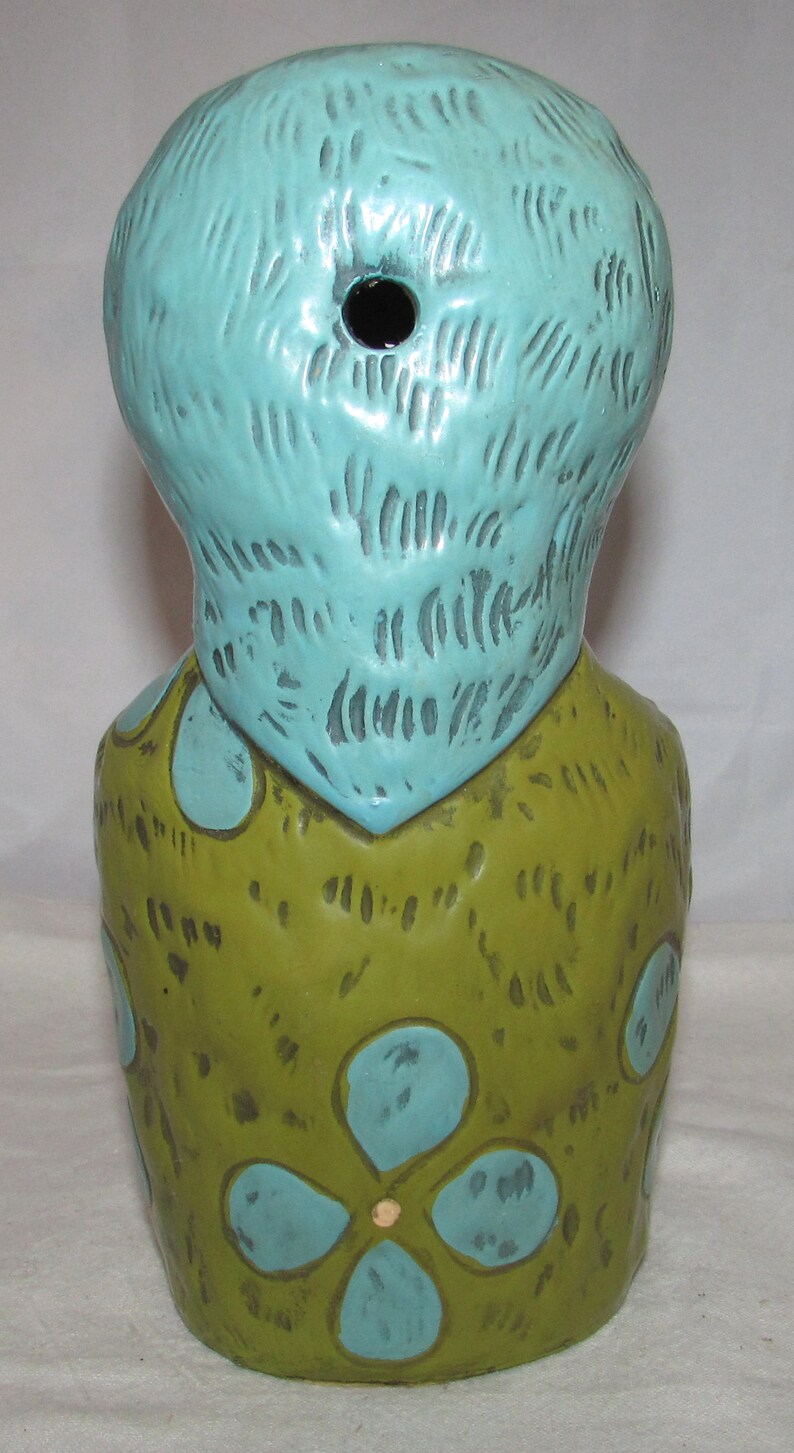 Pu&ograve; includere: Un mug tiki in ceramica con una testa blu e un corpo verde. Il corpo &egrave; decorato con fiori blu.