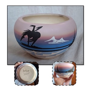 May include: A round ceramic bowl with a pink, blue, and white painted landscape design. The bowl features a black silhouette of a bird and mountains. The interior is white, and the bottom of the bowl has the text "Native Dine!"