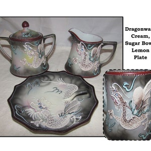 May include: A set of Dragonware china featuring a cream pitcher, sugar bowl, and a lemon plate. Each piece is decorated with a detailed, embossed dragon design in shades of gray, white, and blue.