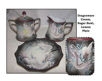 May include: A set of Dragonware china featuring a cream pitcher, sugar bowl, and a lemon plate. Each piece is decorated with a detailed, embossed dragon design in shades of gray, white, and blue.