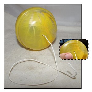 May include: A yellow plastic yo-yo with a white string. The yo-yo has a swirl pattern and the text "The Master" is printed on the bottom.