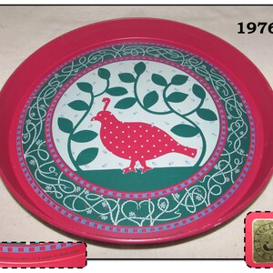 May include: A round, red metal tray with a central design featuring a red bird with white polka dots, green leaves, and a white and green border. The tray has the text "1976" and "McIntire Designs".