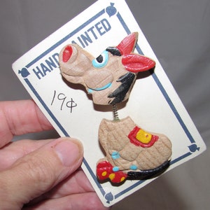May include: A pair of hand-painted wooden buttons featuring a cartoon donkey with red, yellow, blue, and black details. The buttons are attached to a card that reads "HAND PAINTED" and "19¢".