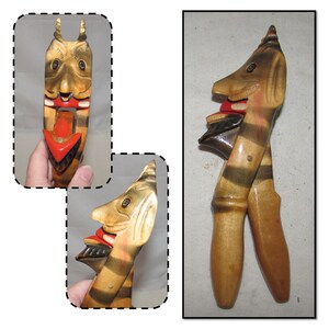 May include: A wooden nutcracker with a carved face and striped body. The nutcracker is painted in shades of brown, black, and red. The mouth of the nutcracker is open, revealing a red tongue and black teeth.