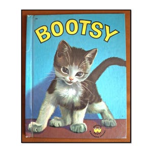 May include: A vintage children's book titled BOOTSY with a light blue cover featuring a brown and white kitten standing on a dark surface. The book includes the Wonder Books Washable Covers logo in the bottom right corner and the number 741.