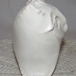 May include: White ceramic sculpture of a stylized head with a textured surface.