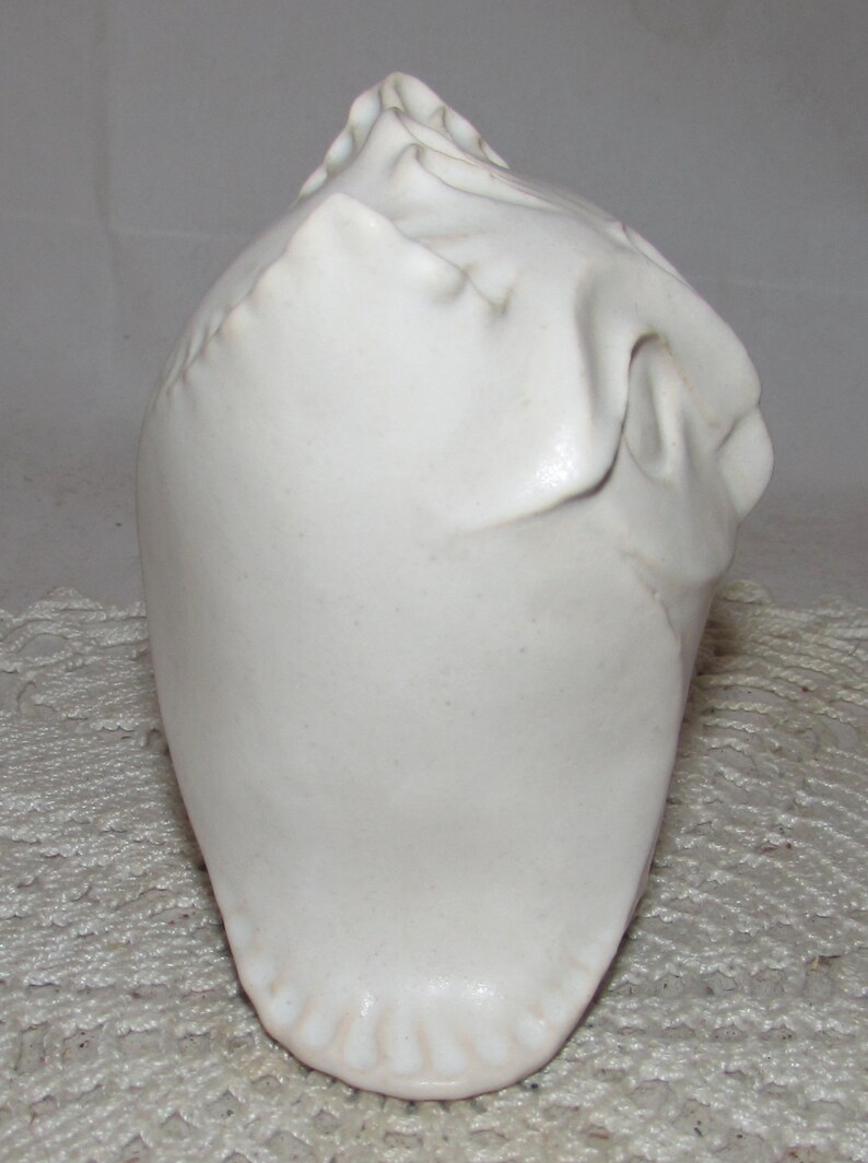 May include: White ceramic sculpture of a stylized head with a textured surface.