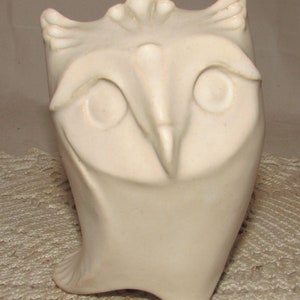 May include: White ceramic owl figurine with a stylized design. The owl has large eyes and a beak.