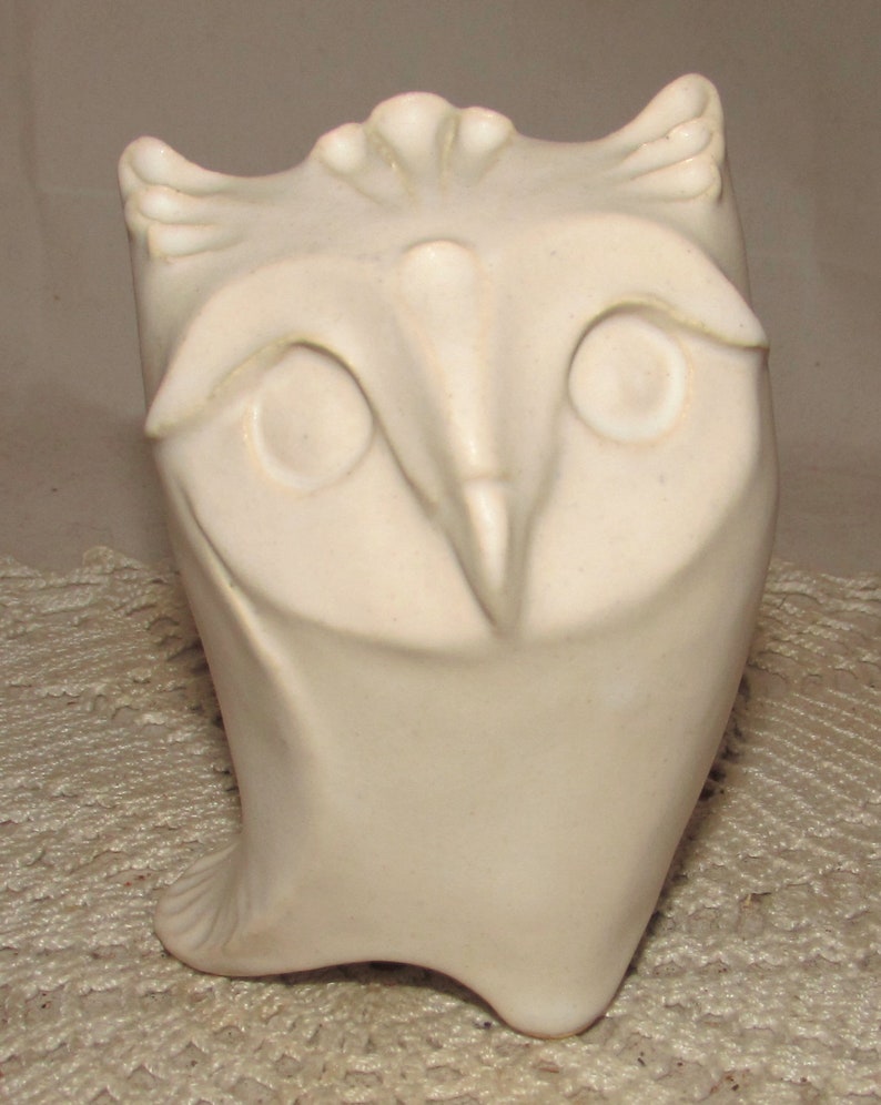 May include: White ceramic owl figurine with a stylized design. The owl has large eyes and a beak.