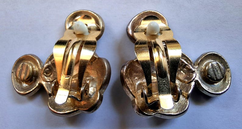 Puede incluir: Un par de pendientes vintage de clip. Los pendientes tienen un acabado met&aacute;lico dorado con un dise&ntilde;o floral. El mecanismo de clip es visible y los pendientes se muestran desde la parte posterior.