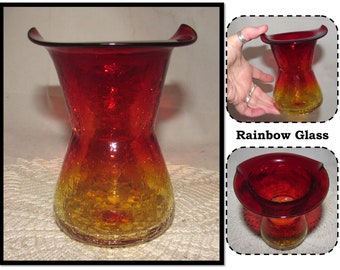 May include: A red and yellow glass vase with a wide, flared top. The vase has a textured surface and a unique, hourglass shape. "Rainbow Glass" is written on the image.