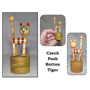 May include: A wooden push-button toy tiger with brown and white stripes. The tiger has a painted face with blue eyes and a red nose. The toy is on a wooden base.