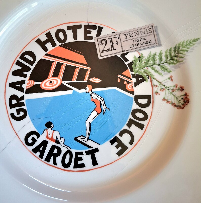 Op de afbeelding: Een wit keramiek bord met een kleurrijk ontwerp met een zwembad, twee figuren en de tekst "Grand Hotel Garot Dolce 2F Tennis Hotel St. George".