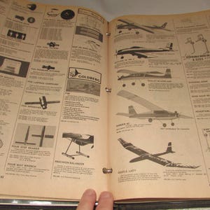 Puede incluir: P&aacute;ginas abiertas de un cat&aacute;logo vintage que muestran dise&ntilde;os de aviones modelo, piezas y accesorios. Las p&aacute;ginas son de color beige con texto e ilustraciones en negro, incluidos diagramas de aviones y componentes. El cat&aacute;logo est&aacute; abierto por una mano.