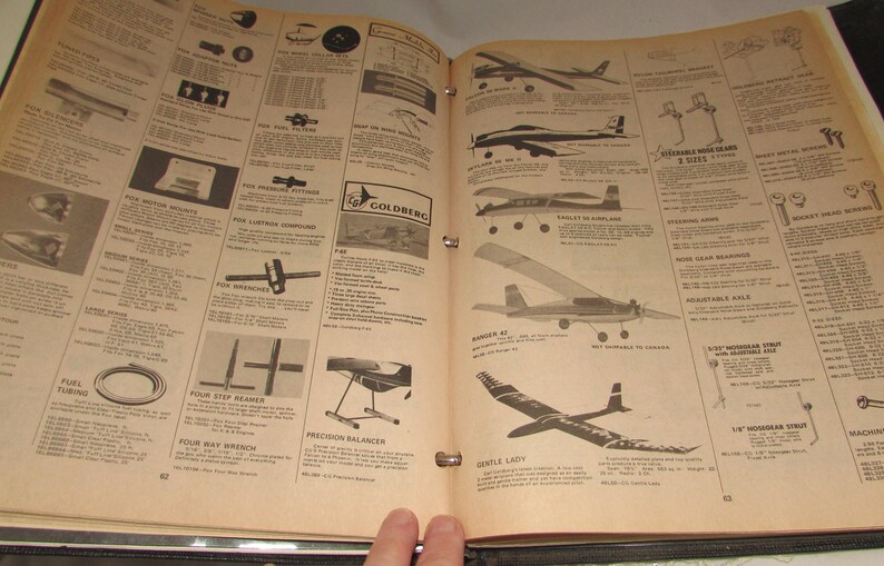 Puede incluir: P&aacute;ginas abiertas de un cat&aacute;logo vintage que muestran dise&ntilde;os de aviones modelo, piezas y accesorios. Las p&aacute;ginas son de color beige con texto e ilustraciones en negro, incluidos diagramas de aviones y componentes. El cat&aacute;logo est&aacute; abierto por una mano.