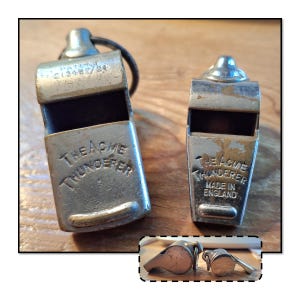 May include: Two vintage metal whistles, "The Acme Thunderer", with visible text. One has a black cord attached. The whistles are silver-toned with some wear. The text "MADE IN ENGLAND" is visible on one whistle.