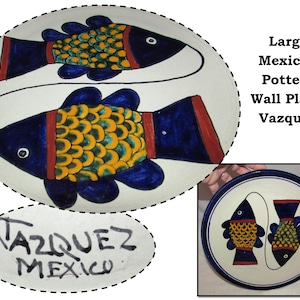 May include: Large Mexican pottery wall plate with two blue fish with yellow and green scales on a white background. The plate is signed "Vazquez Mexico".