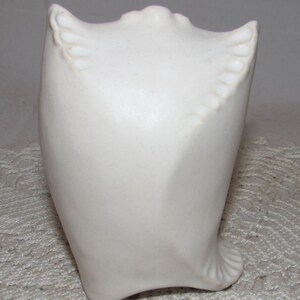 May include: White ceramic owl sculpture with a smooth, rounded body and detailed wings. The owl is perched on a white surface.