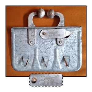 May include: A vintage metal tool with a handle and a series of triangular cutouts. The tool has a rectangular shape with a hinged handle and a small metal plate with text. The metal has a weathered appearance.