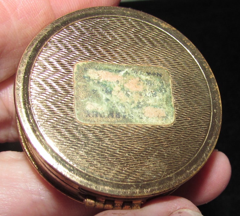 May include: Gold compact with a textured surface and a faded label on the back.