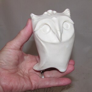 May include: White ceramic owl sculpture with a stylized design. The owl has large eyes and a beak.