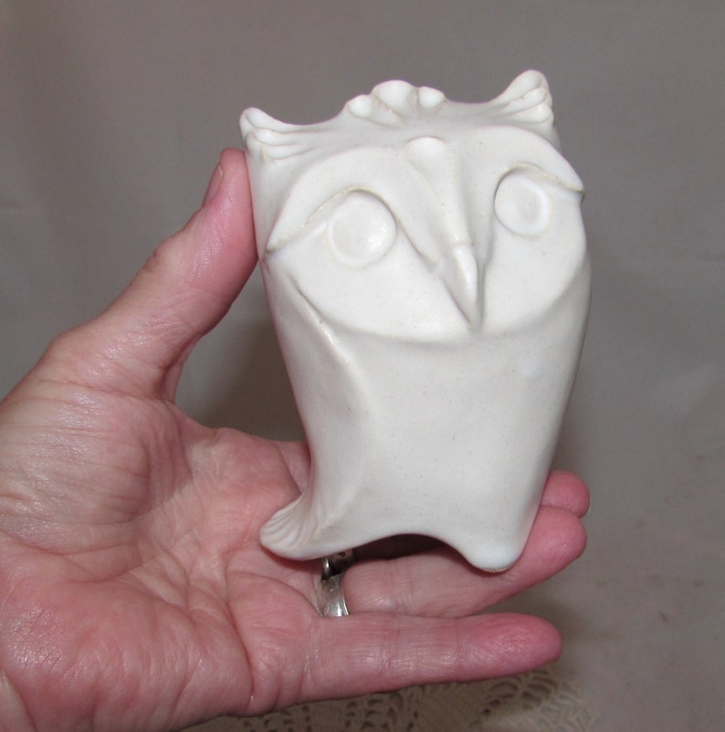 May include: White ceramic owl sculpture with a stylized design. The owl has large eyes and a beak.