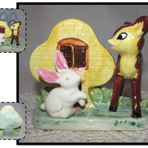 May include: A ceramic pen holder featuring a yellow house with brown windows, a white rabbit with pink ears, and a brown and yellow deer. The base is green with painted grass and foliage. The pen holder has a whimsical, vintage aesthetic.