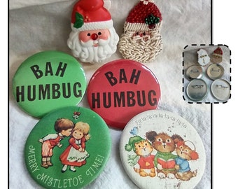 May include: A collection of vintage Christmas pins and brooches. Includes a Santa Claus brooch, a beaded Santa brooch, and several round pins with phrases like "Bah Humbug" and "Merry Mistletoe Time!" in red and green.
