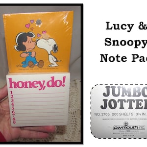 May include: A yellow and pink notepad featuring Lucy and Snoopy from Peanuts. The notepad has 200 sheets and is 3 3/8 inches by 3 3/8 inches. The front of the notepad says "honey, do!" and has a list of numbers 1 through 9. The back of the notepad says "JUMBO JOTTER" and "NO. 2705 200 SHEETS 3 3/8 IN. X 3 3/8 IN."