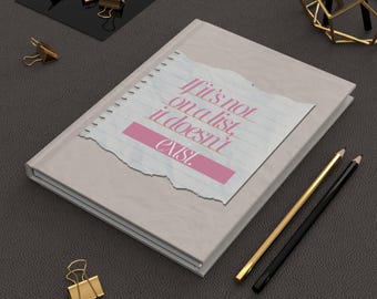 May include: A beige journal with the text "If it's not on a list, it doesn't exist" printed on a torn paper design. Gold and black pencils and gold binder clips are also visible.