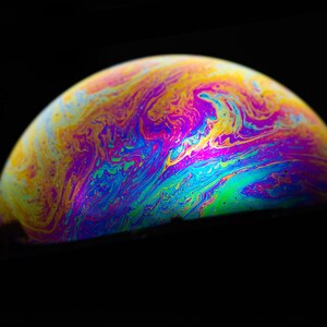 Könnte beinhalten: Nahaufnahme einer bunten, schillernden Seifenblase, die einem Planeten mit wirbelnden Mustern in Blau, Grün, Gelb und Lila ähnelt.