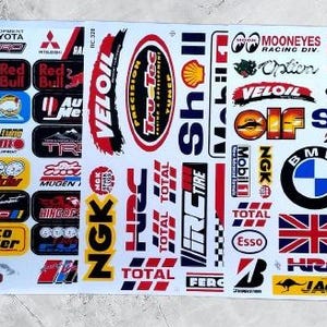 Può includere: Un foglio di adesivi a tema corse e automobilismo. Gli adesivi presentano vari loghi di marchi, tra cui Red Bull, Shell, BMW e Michelin. Gli adesivi sono in vari colori.