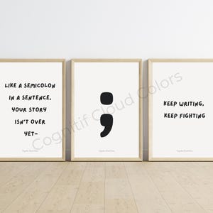 Pode incluir: Três impressões emolduradas com citações inspiradoras e um ponto e vírgula. A primeira impressão diz "Como um ponto e vírgula em uma frase, sua história não acabou." A segunda impressão apresenta um ponto e vírgula preto grande. A terceira impressão diz "Continue escrevendo, continue lutando."