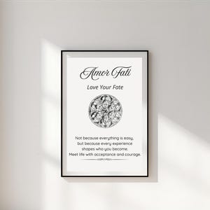 May include: Framed art print with the words "Amor Fati" and "Love Your Fate" in elegant script. The print features a circular, symmetrical design and inspirational text about embracing life's experiences. The black frame contrasts with the white background.