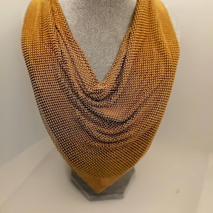 May include: A gold-colored chainmail necklace displayed on a mannequin. The necklace is made of small, interconnected metal rings, creating a delicate and intricate design.