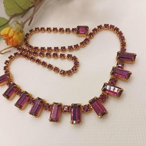 May include: A gold necklace with a chain of small purple rhinestones and a pendant of larger rectangular purple rhinestones.