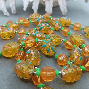Könnte beinhalten: Eine Vintage-Halskette aus Bernstein-Glasperlen mit floralem Design. Die Perlen sind eine Mischung aus runden und ovalen Formen und auf einer silbernen Kette aufgefädelt. Die Halskette ist ein wunderschönes Beispiel für Vintage-Schmuck.