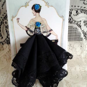 May include: A black lace handkerchief with a vintage illustration of a woman in a black dress and blue flowers on a white background.