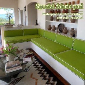 May include: A lime green L-shaped sofa cushion set with white piping. The text on the image reads: Special fabric pad, Waterproof scratch-resistant and stain-resistant. The cushions are placed on a white built-in base in a room.