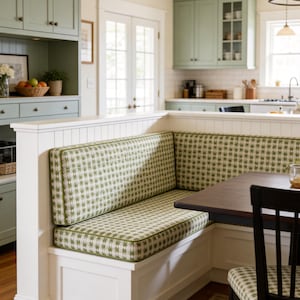 May include: A built-in kitchen bench with a green and white patterned cushion. The bench is part of a white structure with a wooden table and a black chair. The kitchen cabinets are painted in a light green color.
