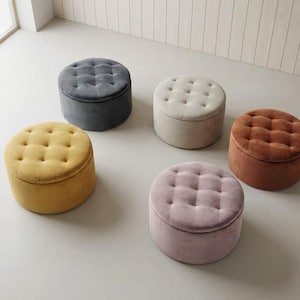 May include: Five round, tufted ottomans upholstered in velvet fabric. The collection includes stools in mustard yellow, dark grey, cream, light pink, and burnt orange. Each piece features a button-tufted top and a cylindrical shape.
