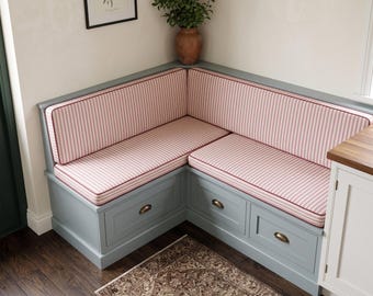 Puede incluir: Un banco esquinero con base de madera azul claro que incluye tres cajones de almacenamiento con tiradores color bronce. El banco cuenta con cojines de asiento y respaldo gruesos y rectangulares tapizados en tela de rayas verticales blancas y rojas.