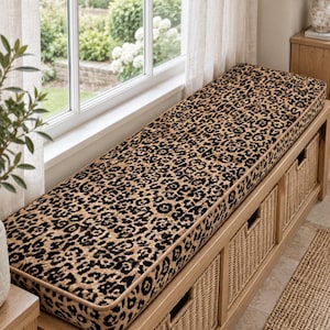 May include: A long rectangular wooden storage bench featuring a thick seat cushion upholstered in a tan and black leopard print fabric. The base of the bench includes three integrated compartments, each containing a woven wicker storage basket.