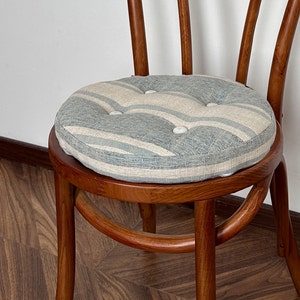 Puede incluir: Una silla de madera con un cojín a rayas azul claro y blanco. El cojín tiene botones blancos.