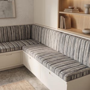 May include: An L-shaped built-in bench with white cabinetry and integrated storage drawers. The bench features thick, rectangular seat and back cushions upholstered in a textured fabric with a vertical striped pattern in shades of gray, black, and white.
