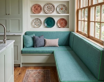 May include: An L-shaped teal bench with bright green piping, three decorative throw pillows, and a runner rug with a faded red pattern. Above the bench, three white shelves display nine ceramic plates in various colors and intricate patterns.