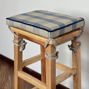 Puede incluir: Un taburete de madera con un cojín a cuadros. El cojín está atado al taburete con lazos de tela azul y blanco.