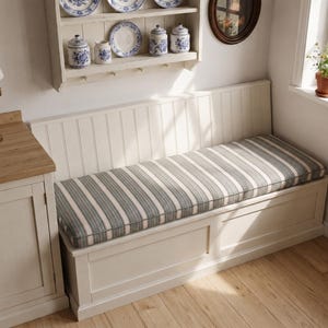 May include: A long, off-white wooden bench with a high, vertical-slat backrest and a rectangular seat cushion featuring a dark grey and white striped pattern. The bench is positioned against a wall, providing a structured seating area.
