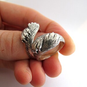 May include: A silver ring shaped like a pair of animal paws wrapped around each other. The ring is detailed with textured fur and claws.